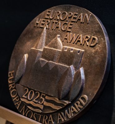 Medalion z brązu z napisami Nagroda Dziedzictwa Europejskiego, Nagroda Europa Nostra i 2025, z wytłoczonym wizerunkiem historycznego budynku z wodą i łukami.