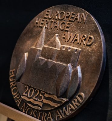 Medalion z brązu z napisami Nagroda Dziedzictwa Europejskiego, Nagroda Europa Nostra i 2025, z wytłoczonym wizerunkiem historycznego budynku z wodą i łukami.