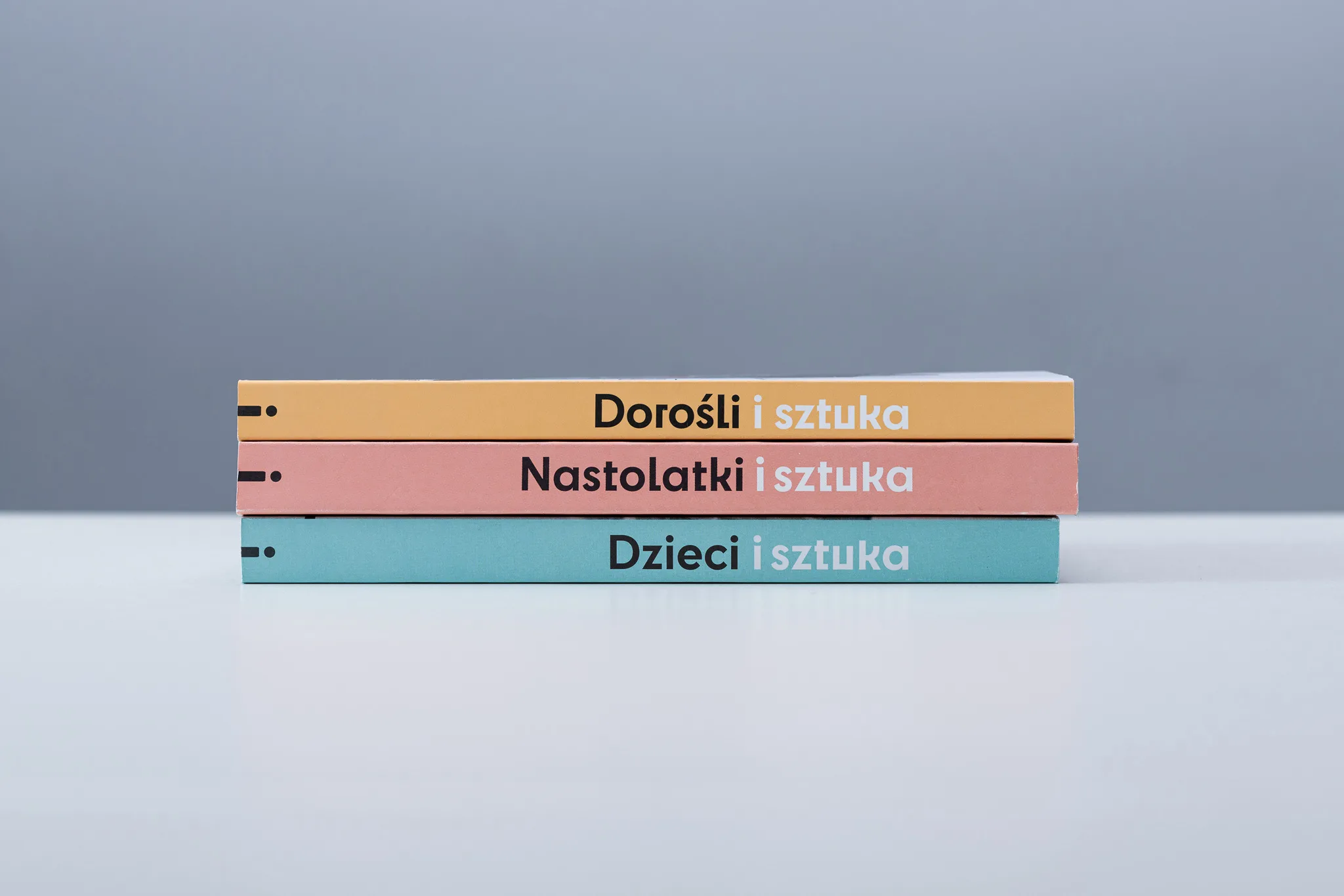 Trzy książki ustawione na stosie, z perspektywy widać kolorowe grzbiety z tytułami