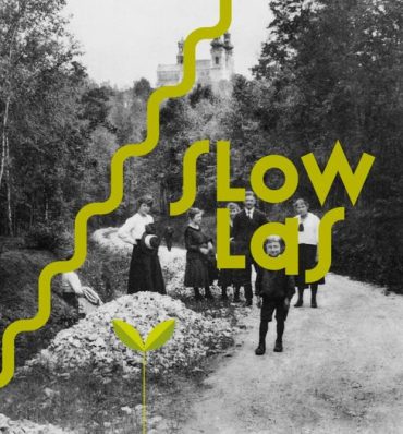 Stara, czarno-biała fotografia z grupą ludzi spacerującą przez las, na zdjęcie nałożony ozdobny, zielony napis "SLOW LAS"