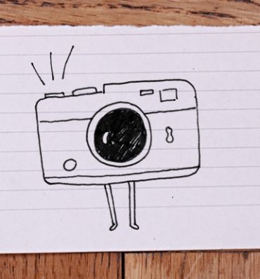 zdjęcie kartki papieru na blacie - na kartce ilustracja aparatu fotograficznego z małymi nóżkami