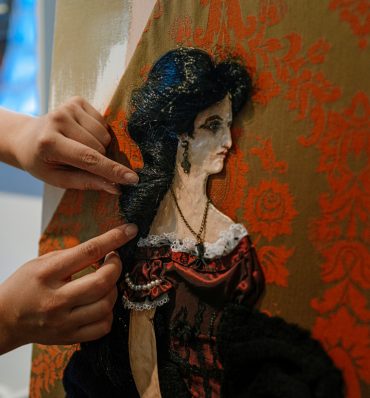 ręce przytrzymują włosy postaci kobiety wyszytej na materiale